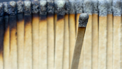 A burnt match head focused against a blurred background of burnt cardboard matches