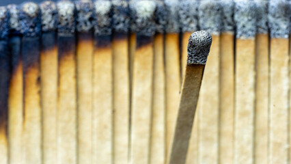 A burnt match head focused against a blurred background of burnt cardboard matches