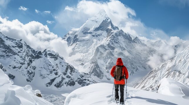 A solitary hiker in a red jacket stands with trekking poles, gazing at a stunning snow-covered mountain peak, embodying adventure and the spirit of exploration.