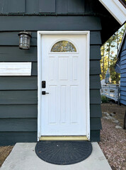 a dark wood house with a white front door with panels - home in rural America - cabin door with lamp, half round window, welcome mat, door plate for address, black lock and door handle