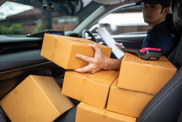 A delivery man wearing a hat and uniform checks the customer's address. Cardboard boxes near delivery truck to customer's home The postman is delivering a parcel.