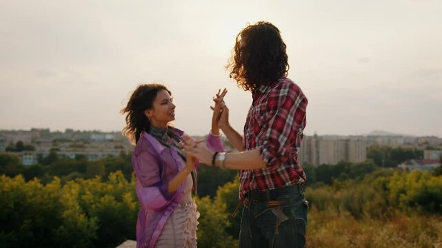 Happy woman and man dancing together at sunset. Positive couple making funny moves during dance outdoor. Female and male hipsters jumping in air. Guy and girl having fun.