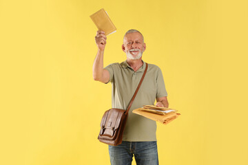 Happy postman with brown bag delivering letters on yellow background