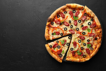 Tasty pizza with dry smoked sausages, olives, pepper and parsley on black table, top view. Space for text