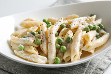 Delicious pasta with green peas and creamy sauce in bowl on table, closeup