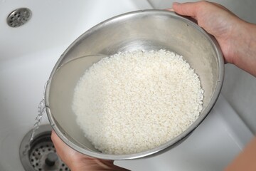 Woman rinsing rice in bowl above sink, closeup