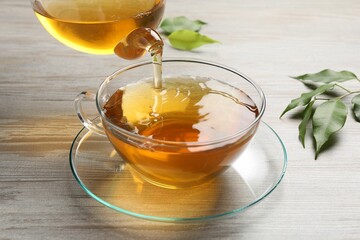 Pouring refreshing green tea into cup at grey wooden table, closeup