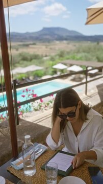 Woman reading menu outdoors in a restaurant in mallorca spain with mountains in the background and swimming pool nearby on a sunny day