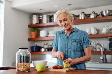 Senior woman, health and home with cutting fruit for breakfast or cooking, vegan diet or nutrition for wellness. Female person, kitchen and knife with apple for relax or retirement, food or muesli