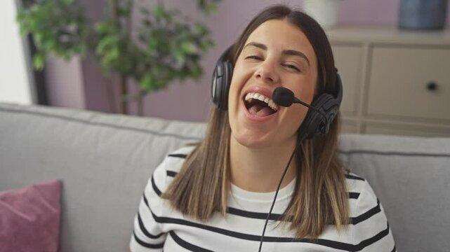 A young, attractive hispanic brunette woman chatting happily wearing a headset in the living room of her home, indicating a relaxed indoor setting.