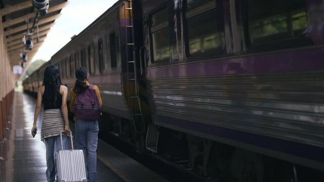Two friends with backpacks and luggage board a train at a station. They walk along the platform, lively chatting and preparing for their journey