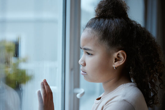 Girl, child and sad at window in house with depression, abandoned or waiting on adoption in foster care. Orphan kid, mental health and lonely or daydreaming of new home with trauma, stress or unhappy