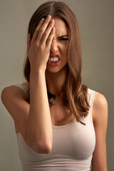 Shout, cover face and portrait of woman in studio with anger, upset and mad reaction. Body language, facial expression and isolated person with hands on eye for stress, unhappy or emoji on background