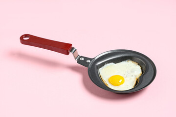 Frying pan with heart-shaped fried egg on pink background