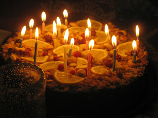 Homemade cake with burning birthday candles in dark room. Cozy home celebration.