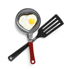 Frying pan with heart-shaped fried egg and spatula on white background