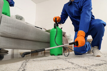 Male worker disinfecting under sofa in room