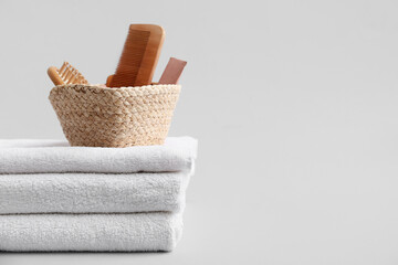Stack of clean soft towels, wicker basket with combs and cosmetic product on white background, closeup