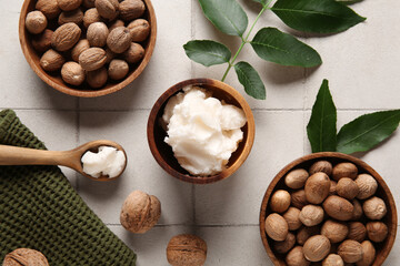 Bowls and spoon of shea butter with nuts on white tile background