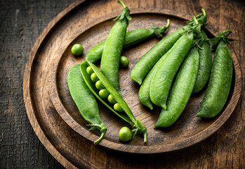 Beautiful young fresh green peas in pods on wooden plates, close-up. Rustic.