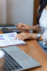 Fototapeta premium Closeup hands of young asian businesswoman pointing on document to checking financial data with calculator while thinking about investment and planning of new startup project for working in cafe