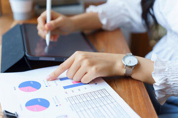 Closeup hands of young asian businesswoman checking finance data on business document and taking notes on tablet while thinking about investment and planning of new startup project to working in cafe