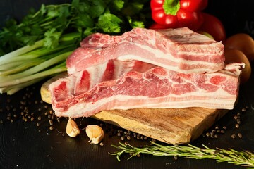 Pieces of raw meat lie on a wooden board surrounded by vegetables and spices. Meat production