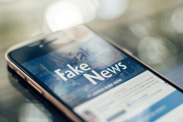Smartphone displaying "Fake News" on screen with blurred background. Media misinformation, digital age, online false information, social media trust, information integrity.