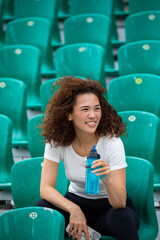 Beautiful curly Asian woman drinks water at the stadium after jogging © kanashkin