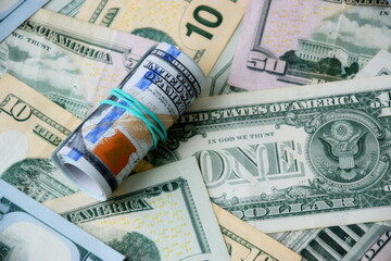 Hundred dollar bills roll lies on big amount of US dollars in different nominations under natural light