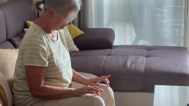 Close up of sad pensive 70s retiree woman put chin on folded palms experiences sentimental longing for period in past looks into distance, sit indoor. Melancholy, retired life, nostalgic mood concept