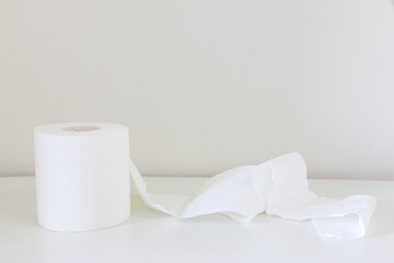 Soft white tissue roll (toilet roll, loo roll, bog roll) slightly unravelled on white table