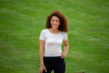 A beautiful curly girl posing in a white T-shirt and black leggings. Against the background of the stadium. Suitable for mockup