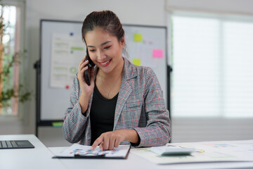 Asian businesswoman in a suit in the office is happy while using a smartphone to contact customers, online, video calls in business finance, marketing, taxes of the company.