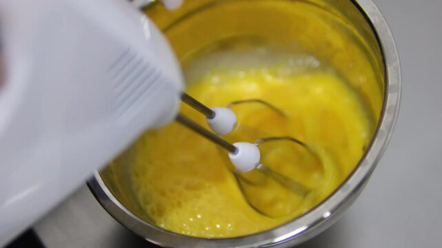 beat eggs with a hand mixer Dipping a switched on mixer into a metal bowl, for whipping eggs.