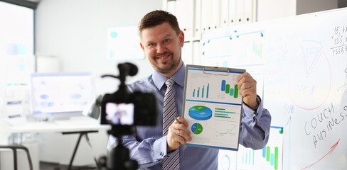 Male in suit and tie show stats graph pad making promo videoblog or photo in office camcorder to tripod portrait. Vlogger selfie solution or finance advisor management information professional concept © H_Ko