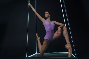 ballerina in a photo studio on a black background in a light led cube shows ballet elements and...