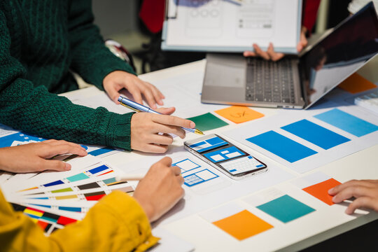 Close-up of hands working on UX/UI design at a desk. Papers with wireframes, prototypes, and mockups detail user flows, personas, and A/B testing, ensuring usability and responsive design.
