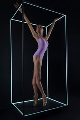 ballerina in a photo studio on a black background in a light led cube shows ballet elements and stretching