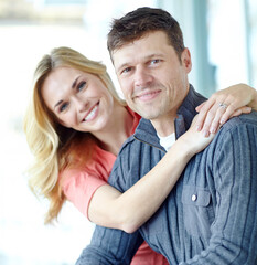 Portrait, hug and happy couple in home for love, relax and loyalty together in lounge. Face, man and woman smile to embrace for support, connection and care for relationship commitment with partner