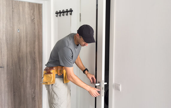 As part of process of installing interior doors in new house, a trim worker uses hammer to strike the door jambs