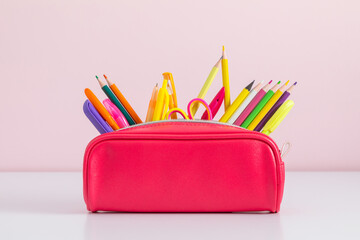 Back to school concept. Pink full pencil case with pencils and pens, scissors, school supplies...