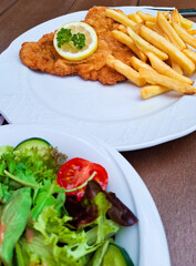 Main meal with breaded meat, pommes frites, white sauce, tomato, salad and fresh mixed vegetables