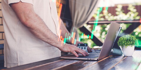 Businessman uses laptop to invest in real estate with growth stability chart. Double exposure