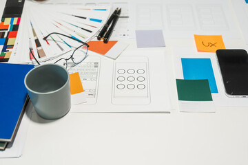 On a desk with paper, a tablet, and a laptop, a digital designer works on user interface (UI) and user experience (UX) concepts, focusing on usability, accessibility, and design principles.