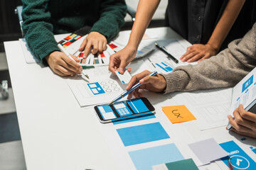 A group of people collaborates around a desk, discussing and reviewing user interface (UI) and user...