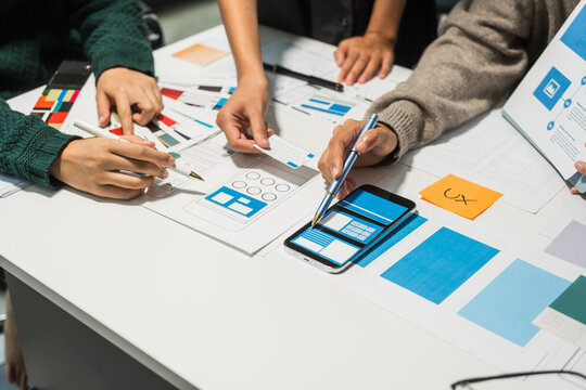 A group of people collaborates around a desk, discussing and reviewing user interface (UI) and user experience (UX) elements. usability, accessibility, and design principles for product development.
