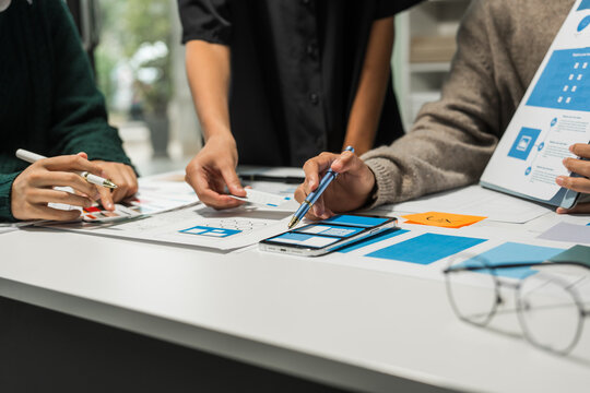 A group of people collaborates around a desk, discussing and reviewing user interface (UI) and user experience (UX) elements. usability, accessibility, and design principles for product development.