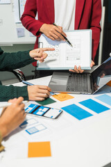 A group of people collaborates around a desk, discussing and reviewing user interface (UI) and user...