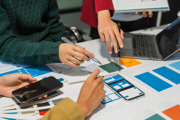 A group of people collaborates around a desk, discussing and reviewing user interface (UI) and user...